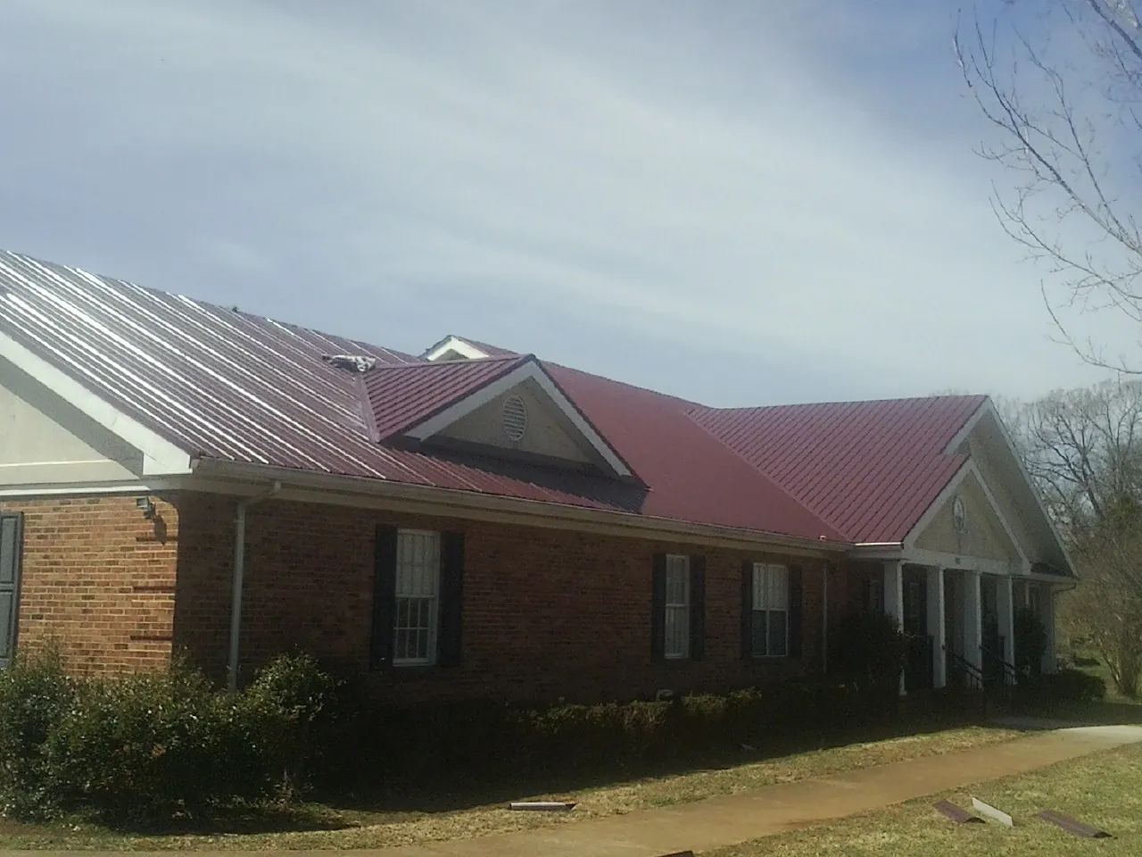 Red metal roof with gabled entries on a long brick building, from a Hail Damage Roof Repair job in Moscow